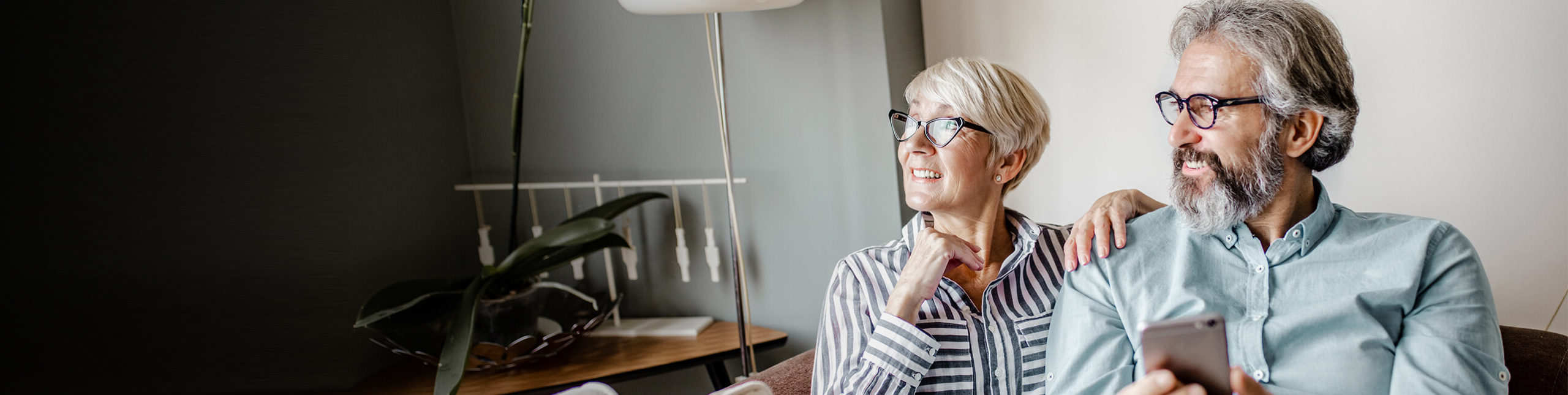 A couple sits on a couch under a blanket, the man holding a smartphone. Social Security Disability benefits provide financial relief when you can't work.