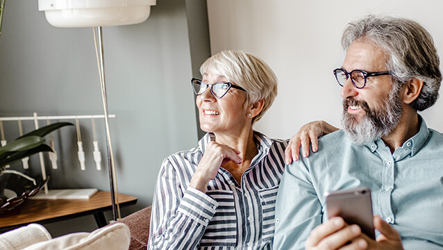 A couple sits on a couch under a blanket, the man holding a smartphone. Social Security Disability benefits provide financial relief when you can't work.