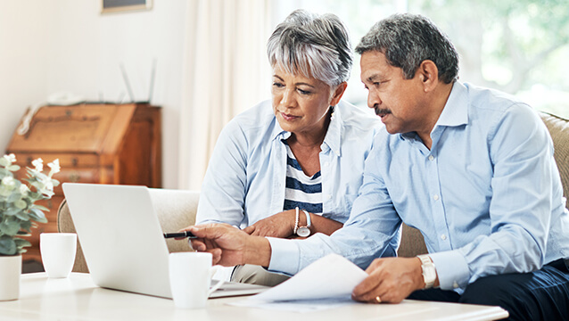 A man and woman sit on a coach, looking at a laptop and papers on a coffee table. It takes work to apply for Social Security Disability benefits.