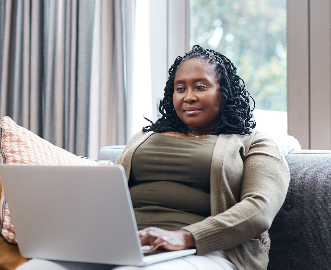 A woman sits on a couch typing on a laptop computer.