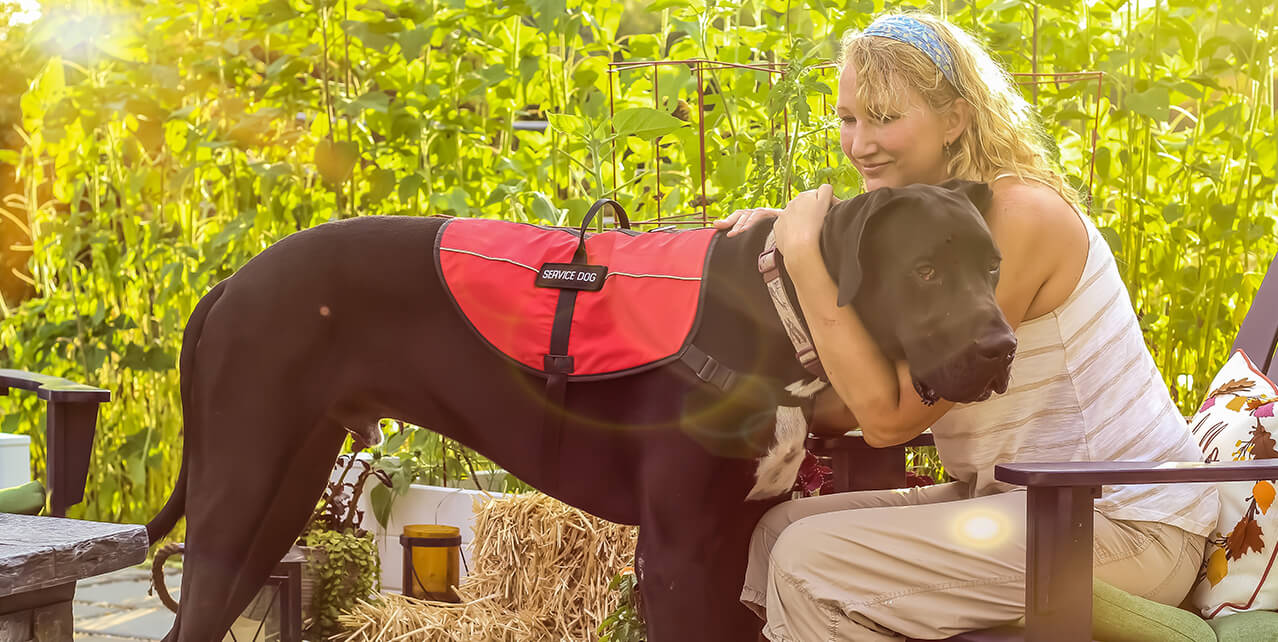 A woman sits in an outdoor patio, hugging a large service dog. You can get Social Security Disability (SSD) for multiple sclerosis.