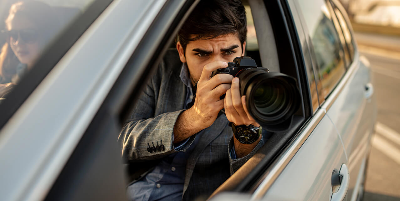 A man sits in a car, taking a picture with a long lens. Social Security can conduct surveillance on you to decide whether to continue your disability benefits.