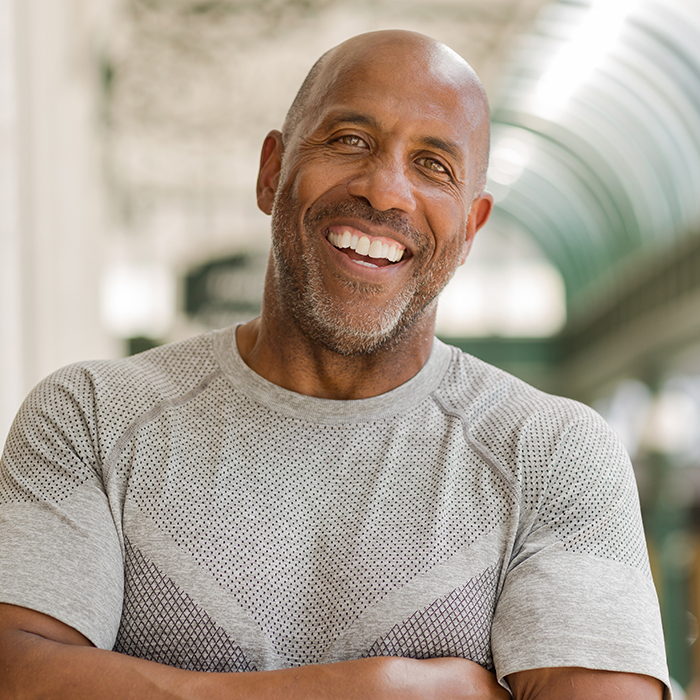 A man stands in a public space with his arms crossed, smiling at the camera.