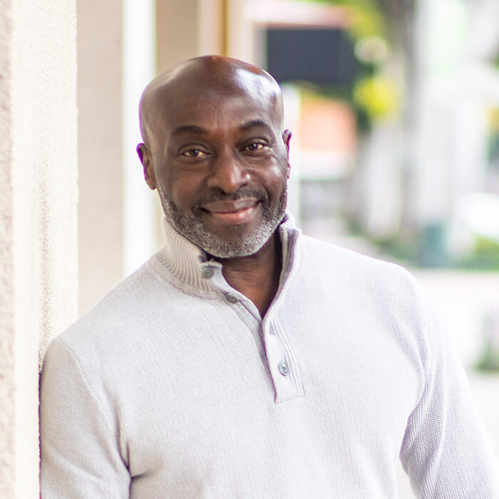 A man leans against a building, smiling.